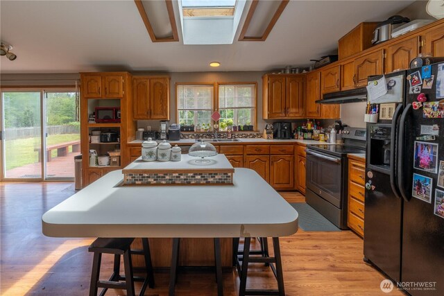 1822 W Devanny Ln, Port Angeles, WA 98363 - kitchen with black fridge, stainless steel electric stove, under cabinet range hood, brown cabinetry, and a center island