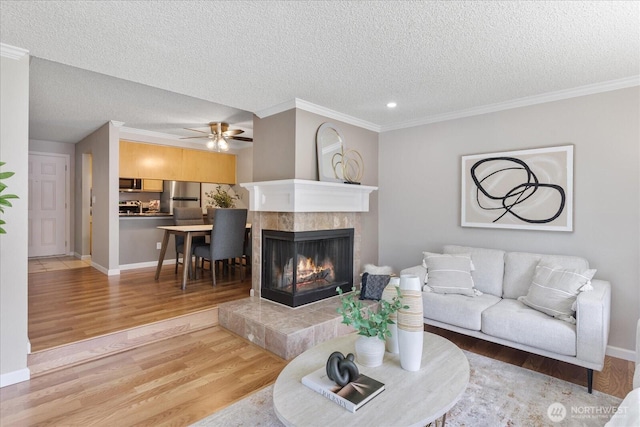 13009 E Gibson Rd Unit Q130, Everett, WA 98204 - living room featuring light wood finished floors, a textured ceiling, a tiled fireplace, ornamental molding, and a ceiling fan