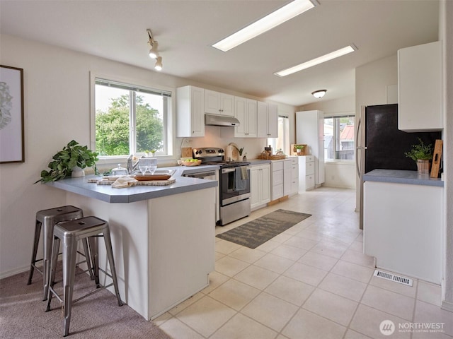 7127 Ortelius Dr, Ilwaco, WA 98624 - kitchen featuring stainless steel range, under cabinet range hood, a peninsula, white cabinets, and a kitchen breakfast bar