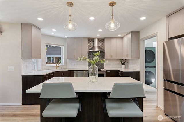 1361 E Old Ranch Rd, Allyn, WA 98524 - kitchen with appliances with stainless steel finishes, estacked washer and dryer, wall chimney range hood, light countertops, and a kitchen breakfast bar