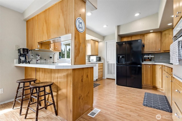 119 Oyler Way, Ethel, WA 98542 - kitchen with black refrigerator with ice dispenser, light wood-style flooring, a peninsula, tile countertops, and a kitchen bar