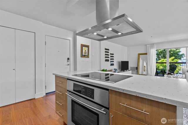 500 5th Ave W Unit 501, Seattle, WA 98119 - kitchen with oven, wall chimney range hood, black electric stovetop, open floor plan, and light stone counters