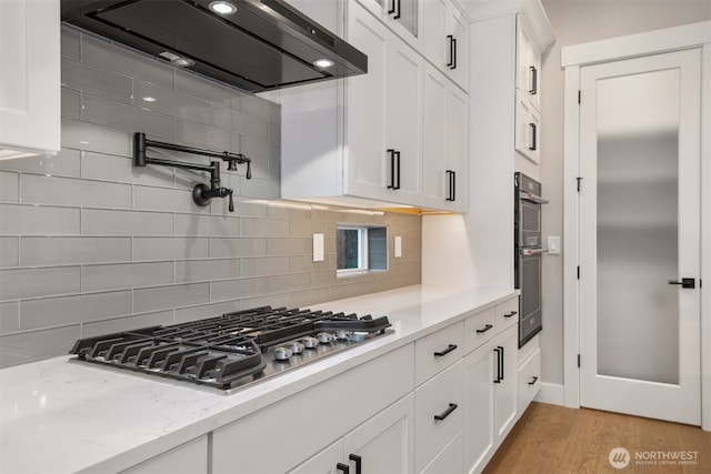 7547 S 130th Pl, Seattle, WA 98178 - kitchen featuring ventilation hood, white cabinets, appliances with stainless steel finishes, light wood-style flooring, and tasteful backsplash