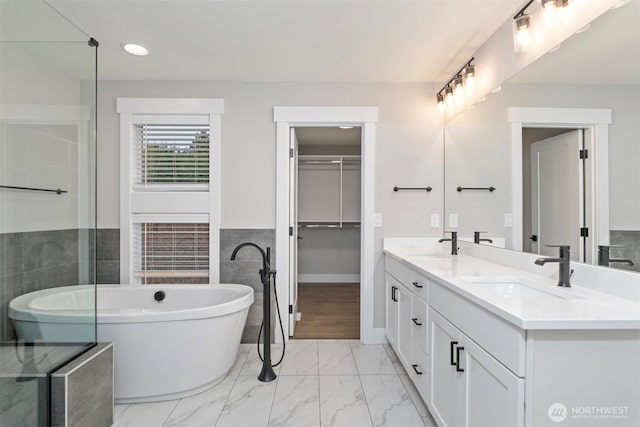 7547 S 130th Pl, Seattle, WA 98178 - full bathroom featuring double vanity, a soaking tub, marble look tile flooring, tile walls, and a spacious closet