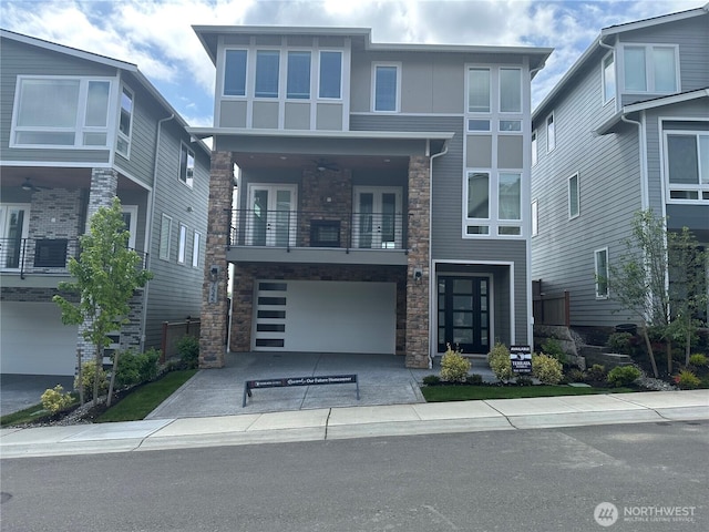7545 S 129th Pl, Seattle, WA 98178 - contemporary house with a balcony, stone siding, an attached garage, driveway, and french doors
