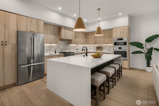 12833 NE 91st St, Kirkland, WA 98033 - kitchen featuring stainless steel appliances, light wood-style flooring, a kitchen bar, tasteful backsplash, and a kitchen island with sink