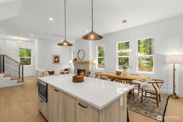 12837 NE 91st St, Kirkland, WA 98033 - kitchen featuring stainless steel microwave, light wood-type flooring, a fireplace, light brown cabinetry, and a center island