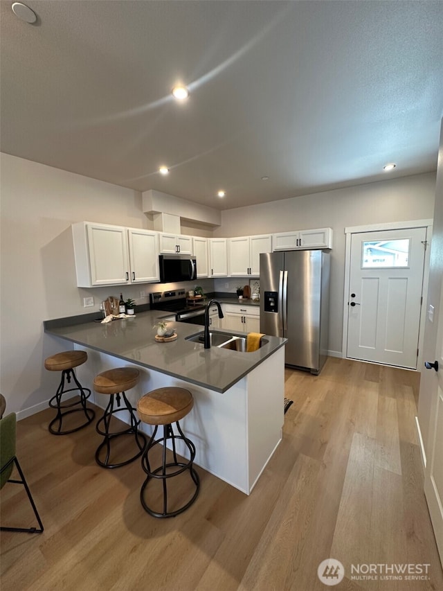 1712 Sunup Loop, Bellingham, WA 98226 - kitchen with appliances with stainless steel finishes, light wood-type flooring, a peninsula, dark countertops, and recessed lighting