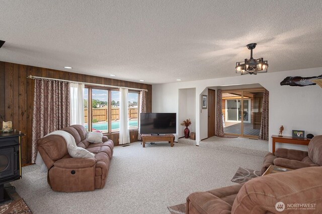 710 S Mckinney Rd, Othello, WA 99344 - carpeted living area with a wood stove, a textured ceiling, a chandelier, recessed lighting, and wood walls