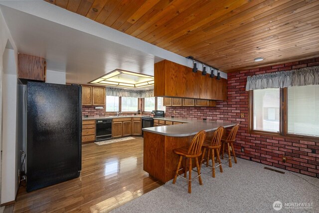 710 S Mckinney Rd, Othello, WA 99344 - kitchen featuring black appliances, a peninsula, brown cabinetry, wood ceiling, and brick wall