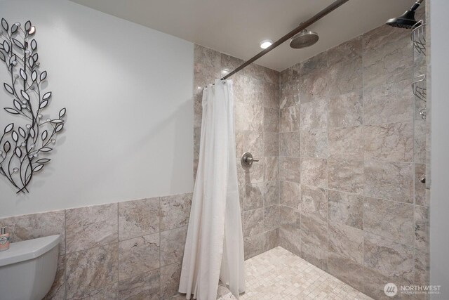 710 S Mckinney Rd, Othello, WA 99344 - full bathroom featuring toilet, tiled shower, tile walls, and a wainscoted wall