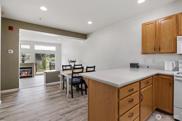2311 Milton Way Unit E, Milton, WA 98354 - kitchen featuring light wood-style floors, recessed lighting, white appliances, a glass covered fireplace, and a peninsula