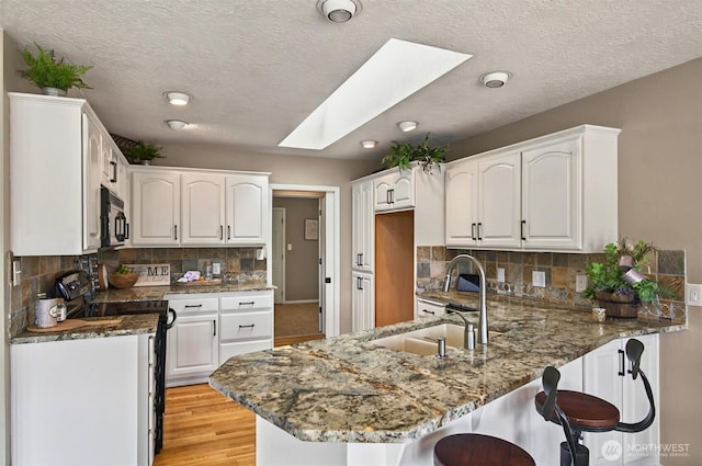293 State Route 409, Cathlamet, WA 98612 - kitchen with electric range oven, a peninsula, black microwave, a sink, and a skylight