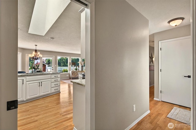 293 State Route 409, Cathlamet, WA 98612 - hallway featuring light wood-style floors, a chandelier, a textured ceiling, baseboards, and a skylight
