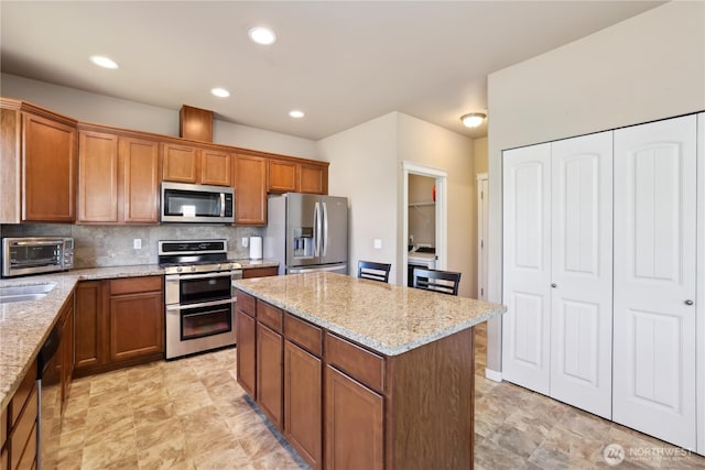 9831 198th St E, Graham, WA 98338 - kitchen with appliances with stainless steel finishes, a kitchen island, brown cabinetry, light stone countertops, and recessed lighting