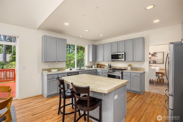 23600 Dunbar Pl NW, Poulsbo, WA 98370 - kitchen with stainless steel appliances, gray cabinets, tile counters, light wood-style floors, and a breakfast bar