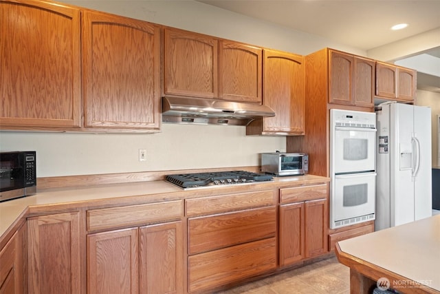 14647 NW Honeyhill Loop, Seabeck, WA 98380 - kitchen with appliances with stainless steel finishes, under cabinet range hood, light countertops, recessed lighting, and brown cabinetry
