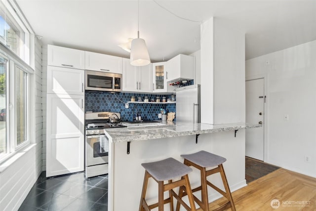 22 John St Unit 10, Seattle, WA 98109 - kitchen featuring stainless steel appliances, a breakfast bar area, light stone countertops, glass insert cabinets, and backsplash