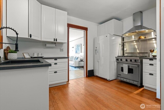3526 Ashworth Ave N, Seattle, WA 98103 - kitchen featuring white refrigerator with ice dispenser, wall chimney exhaust hood, premium range, dark countertops, and light wood-style floors