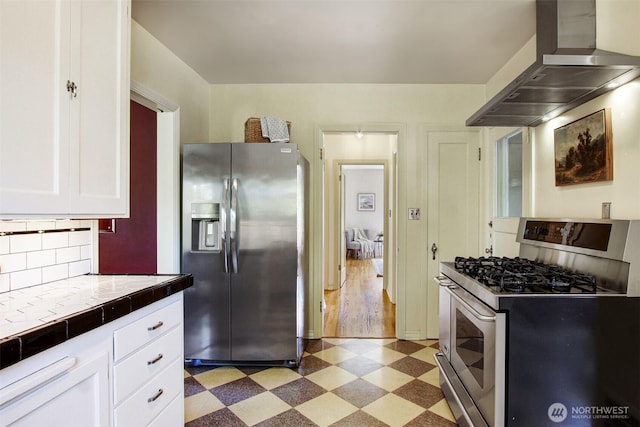 1635 46th Ave SW, Seattle, WA 98116 - kitchen featuring stainless steel appliances, light flooring, wall chimney exhaust hood, tile countertops, and white cabinets