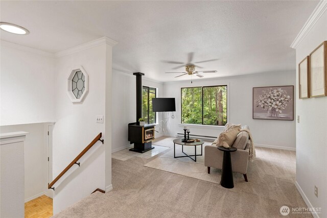 60 E Christmas Tree Pl, Belfair, WA 98528 - carpeted living area with ceiling fan, a wood stove, baseboards, a baseboard heating unit, and crown molding