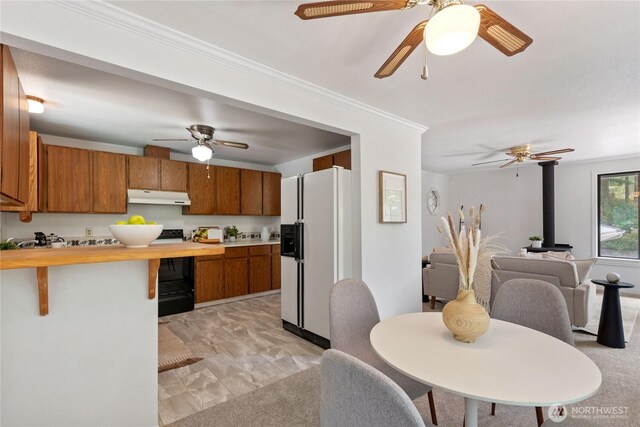 60 E Christmas Tree Pl, Belfair, WA 98528 - kitchen with white fridge with ice dispenser, under cabinet range hood, brown cabinets, a ceiling fan, and ornamental molding
