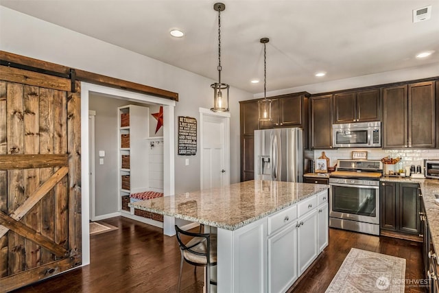 912 77th Dr SE, Lake Stevens, WA 98258 - kitchen featuring appliances with stainless steel finishes, light stone countertops, dark brown cabinets, a barn door, and a kitchen island