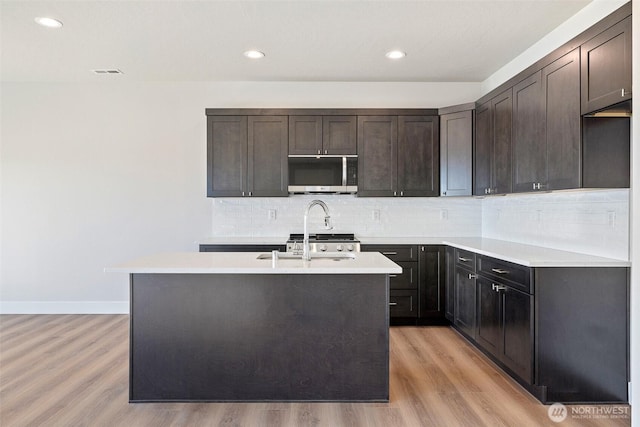 4247 W Sandy Ct, Moses Lake, WA 98837 - kitchen with stainless steel microwave, light wood finished floors, light countertops, tasteful backsplash, and a kitchen island with sink