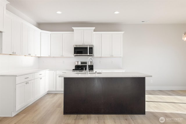 4235 W Sandy Ct, Moses Lake, WA 98837 - kitchen with stainless steel appliances, light wood-style flooring, tasteful backsplash, a sink, and a kitchen island with sink