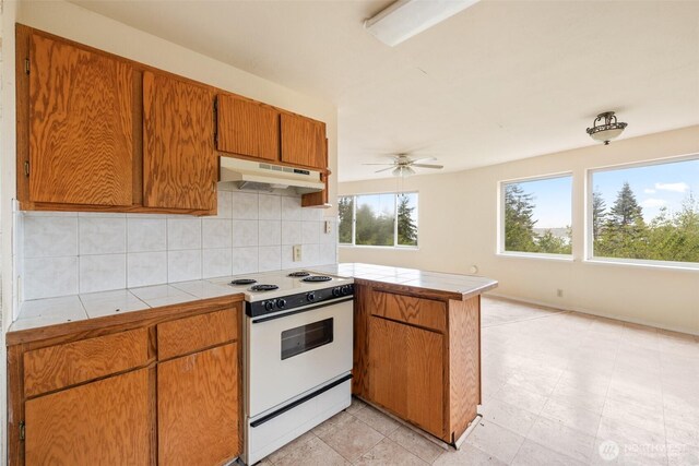 300 N St, Sequim, WA 98382 - kitchen featuring white electric stove, under cabinet range hood, a peninsula, tile countertops, and decorative backsplash