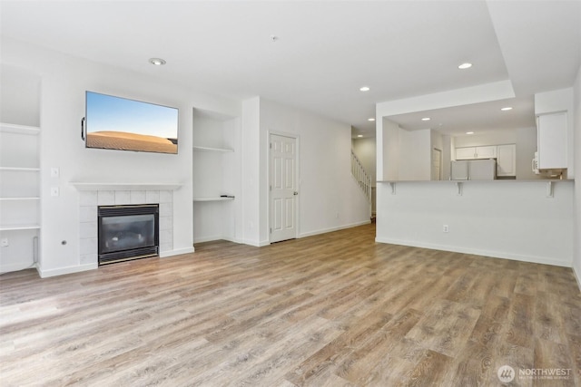 21616 9th Ave SE Unit C-105, Bothell, WA 98021 - unfurnished living room featuring built in features, recessed lighting, light wood-style flooring, a tile fireplace, and stairs