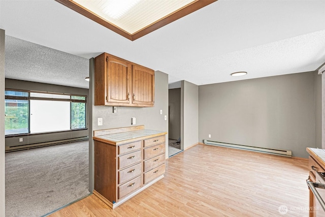 7391 E Grandview St, Port Orchard, WA 98366 - kitchen with baseboard heating, tile counters, light wood-type flooring, a textured ceiling, and brown cabinetry