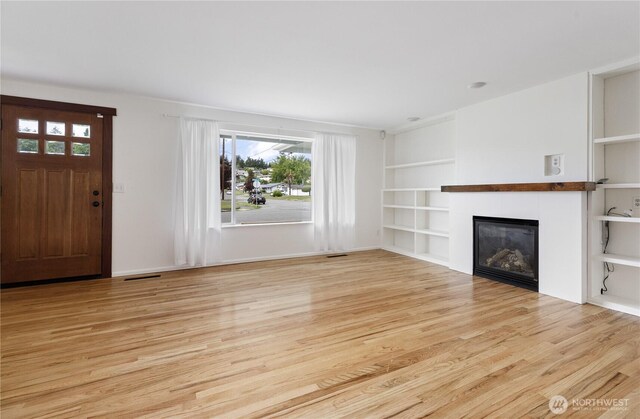 1020 SW Bowmer St, Oak Harbor, WA 98277 - unfurnished living room featuring a glass covered fireplace, light wood-type flooring, built in shelves, and baseboards