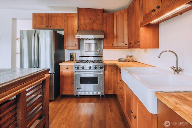 9202 3rd Ave NW, Seattle, WA 98117 - kitchen featuring stainless steel appliances, wall chimney range hood, wood counters, and brown cabinetry