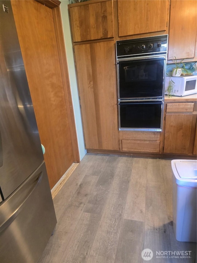 208 N Broadway St, Westport, WA 98595 - kitchen with white microwave, freestanding refrigerator, light wood-type flooring, and brown cabinetry