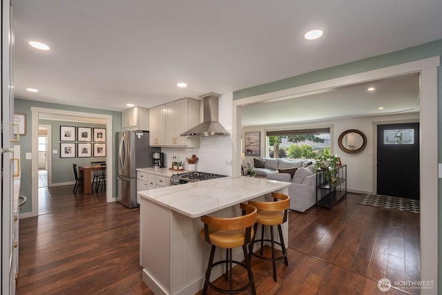 12009 NW Dodson Rd, Ephrata, WA 98823 - kitchen with wall chimney exhaust hood, stainless steel appliances, dark wood-style flooring, a kitchen breakfast bar, and light stone counters
