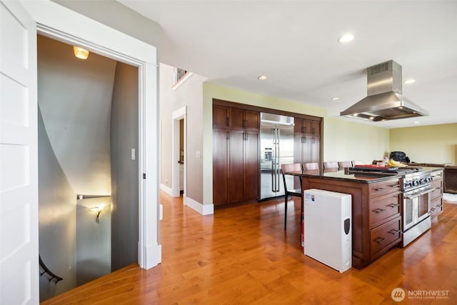 699 Lehman Dr, Camano Island, WA 98282 - kitchen featuring high end appliances, island exhaust hood, dark countertops, light wood-style floors, and a breakfast bar