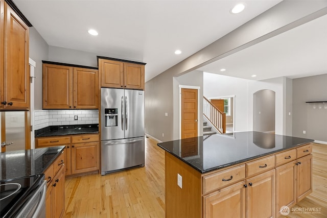 13123 320th Street Ct E, Graham, WA 98338 - kitchen with stainless steel refrigerator with ice dispenser, light wood finished floors, arched walkways, decorative backsplash, and dark stone counters