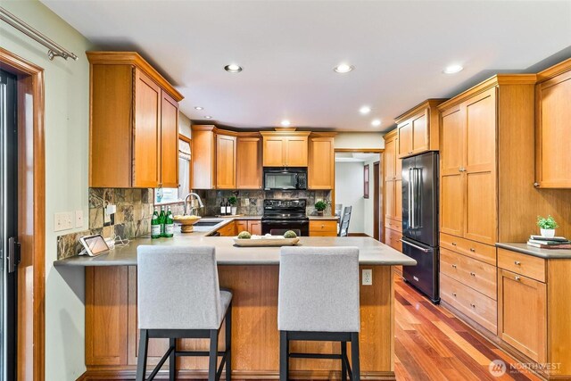 16515 126th Ave NE, Woodinville, WA 98072 - kitchen with black appliances, light wood finished floors, a sink, a peninsula, and decorative backsplash