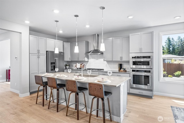 29215 217th Ct SE, Black Diamond, WA 98010 - kitchen featuring stainless steel appliances, wall chimney exhaust hood, baseboards, light wood finished floors, and a kitchen bar
