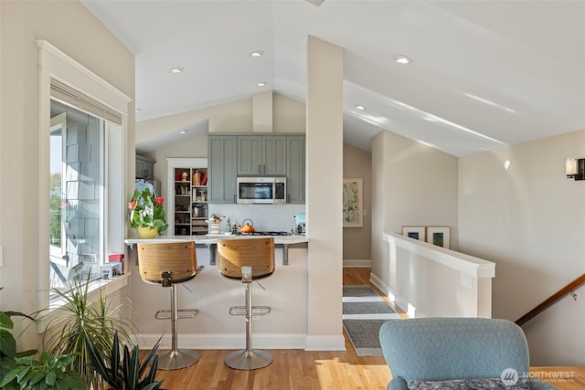 656 Daley St Unit 102, Edmonds, WA 98020 - kitchen with stainless steel microwave, vaulted ceiling, light wood-type flooring, a kitchen breakfast bar, and a peninsula
