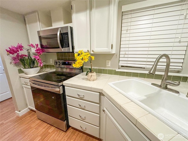 18528 20th Dr SE, Bothell, WA 98012 - kitchen with stainless steel appliances, a sink, tile counters, white cabinetry, and light wood-style floors
