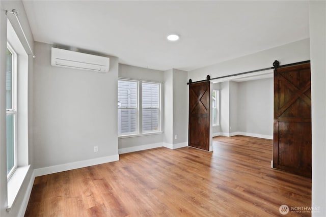 45885 Division St, Concrete, WA 98237 - unfurnished bedroom with a wall unit AC, a barn door, light wood finished floors, and baseboards