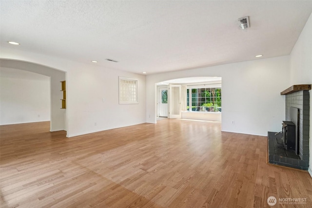 11112 E Riverside Dr, Bothell, WA 98011 - unfurnished living room featuring arched walkways, light wood finished floors, a brick fireplace, and recessed lighting
