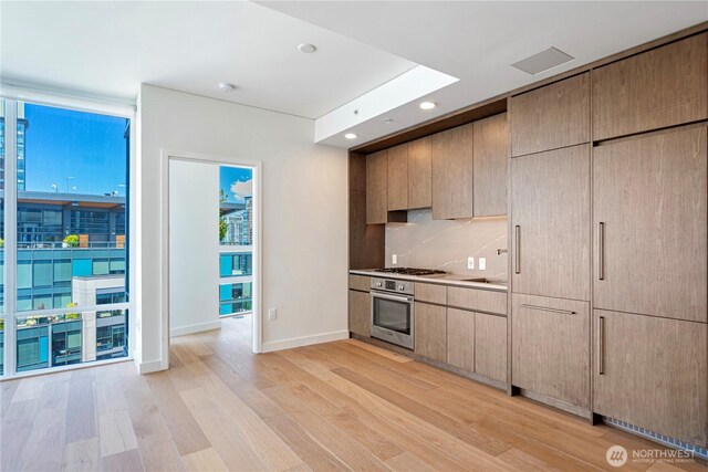 121 Stewart St Unit 2507, Seattle, WA 98101 - kitchen with oven, light wood-type flooring, tasteful backsplash, expansive windows, and baseboards