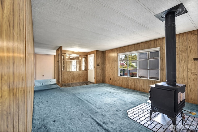 7300 32nd Ave NE Unit 5, Olympia, WA 98516 - unfurnished living room with a wood stove, wood walls, carpet flooring, and a textured ceiling