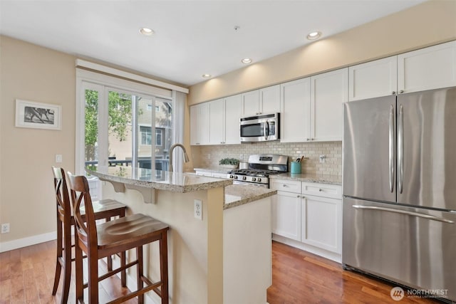 11800 SE 4th Pl Unit 203, Bellevue, WA 98005 - kitchen with stainless steel appliances, decorative backsplash, a breakfast bar, light wood finished floors, and light stone countertops
