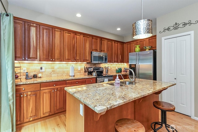 7623 152nd St SE, Snohomish, WA 98296 - kitchen with stainless steel appliances, a sink, light wood-style flooring, light stone counters, and a kitchen bar