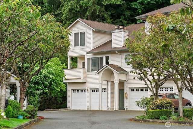 8828 238th St SW Unit D-1, Edmonds, WA 98026 - view of front of house featuring a garage, a balcony, asphalt driveway, a shingled roof, and a chimney