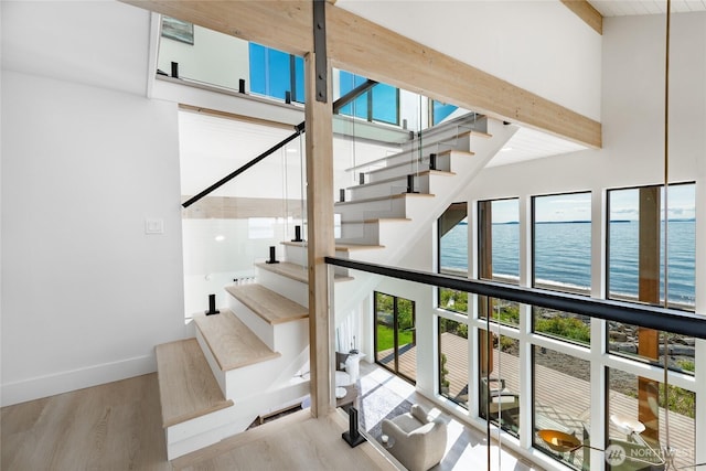 4489 Sucia Dr, Ferndale, WA 98248 - staircase featuring wood finished floors, a water view, a towering ceiling, beamed ceiling, and baseboards